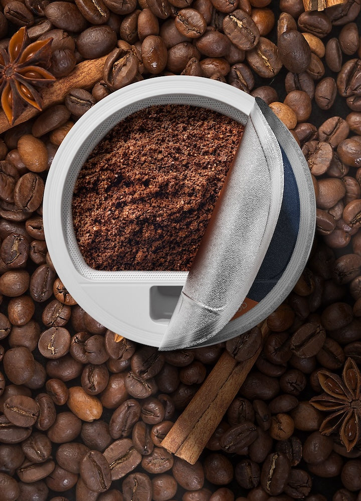 Close-up of ground coffee in a metal filter basket, surrounded by whole coffee beans, cinnamon sticks, and star anise, depicting the rich and aromatic qualities of the FLEX coffee line.